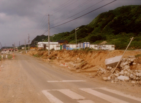 津波によって崩れたのり面と災害後に建てられた仮設住宅（稲穂地区）